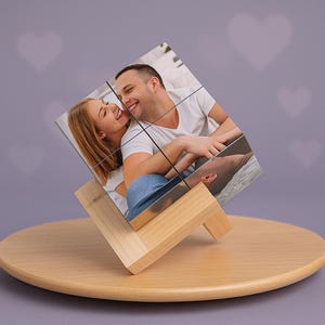 Könnte beinhalten: Ein Fotowürfel mit einem Paar, präsentiert auf einem Holzständer. Der Würfel besteht aus neun Quadraten, die jeweils einen Teil des Fotos zeigen. Der Ständer ist aus hellem Holz gefertigt und steht auf einer runden Holzbasis.
