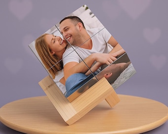 May include: A photo cube featuring a couple, displayed on a wooden stand. The cube is composed of nine individual squares, each displaying a portion of the photograph. The stand is made of light-colored wood and sits on a round wooden base.
