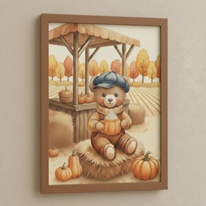 May include: A framed watercolor print of a teddy bear in a blue cap and scarf, holding a pumpkin-shaped mug. The bear sits on a hay bale in a fall scene with pumpkins, a wooden stand, and autumn trees. The artwork is in a brown frame.