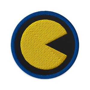 以下が含まれることがあります： 青い縁取りのある黄色のパックマンのキャラクターが黒い布のパッチに刺繍されています