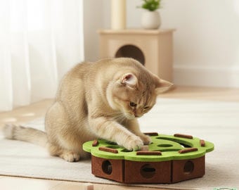 May include: A golden-brown cat plays with a brown and green cat toy. The toy is a hexagonal shape with a green top and brown sides. A small wooden cube sits on the floor near the toy. The cat is focused on the toy.