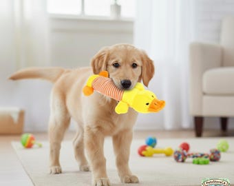 May include: A golden retriever puppy holding a yellow and orange plush duck toy in its mouth. The toy has a striped body and a duck head with an orange beak. Other dog toys are scattered on the floor.