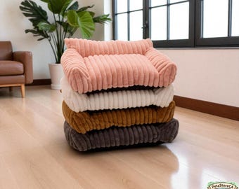 May include: A stack of four pet beds in varying colors: light pink, white, brown, and gray. Each bed has a corduroy texture and a rectangular shape with raised sides, resembling a small sofa for pets.