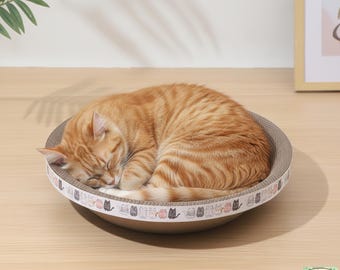 May include: An orange tabby cat curled up asleep in a round, beige cat bed. The bed has a patterned border with cat illustrations. The cat bed is on a light brown surface.