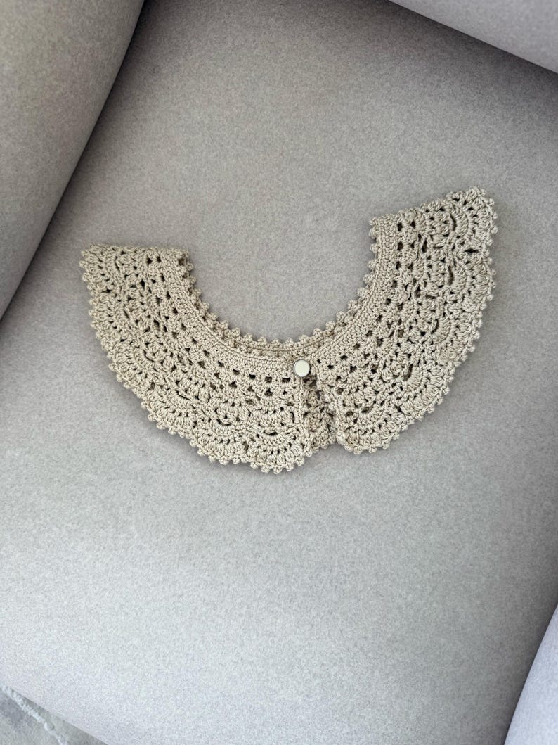 May include: A beige crocheted collar with a scalloped edge and a button fastening. The collar features a delicate, open-weave crochet design. A vintage-style accessory.
