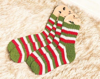 Peut inclure: Une paire de chaussettes à rayures vertes, rouges et blanches. Les chaussettes sont en tricot et sont présentées sur une surface moelleuse de couleur claire. Les chaussettes ont un design classique et festif.