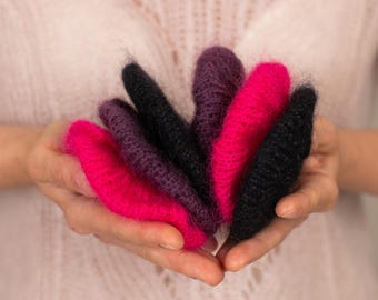 May include: A collection of colorful, hand-knitted items in shades of fuchsia, black, and purple. The items are held in open hands, showcasing the texture and vibrant colors of the yarn. The items appear to be small, possibly fingerless gloves or decorative pieces.