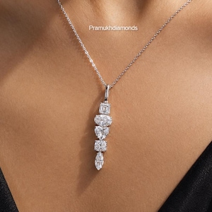 Puede incluir: Un collar de tono plateado con un colgante vertical compuesto por cinco piedras preciosas transparentes de diferentes cortes, incluyendo formas de esmeralda, óvalo, corazón, cuadrado y marquesa. El texto Pramukhdiamonds es visible.