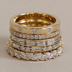 Op de afbeelding: Een stapel van vijf gouden ringen met diverse diamantzettingen. De bovenste ring heeft verzonken ronde diamanten, gevolgd door een pavé-band, een baguette-geslepen eternity-band, een band met ronde en baguette-diamanten en een marquise-geslepen eternity-band.