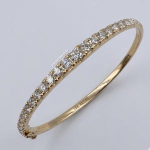 Könnte beinhalten: Ein goldener Armreif mit einer Reihe kleiner, runder Diamanten. Das Armband ist mit "18K AU 750" gekennzeichnet. Die Diamanten sind eng gesetzt und erzeugen ein durchgehendes Funkeln. Ein klassisches Schmuckstück.