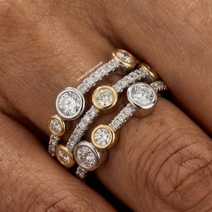 Puede incluir: Primer plano de varios anillos de diamantes. Los anillos combinan oro blanco y amarillo, con varios tamaños de diamantes. Las bandas están incrustadas con pequeños diamantes, y los diamantes más grandes están engastados en bisel.