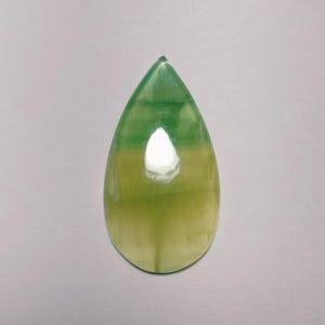 May include: A teardrop-shaped gemstone with a gradient of green and yellow hues. The polished stone has a glossy finish and a pointed top. The color transitions from a deep green at the top to a pale yellow at the base.