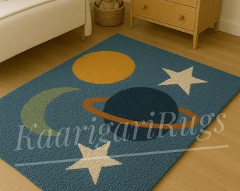 May include: Blue rug with a celestial design featuring a yellow sun, a planet with rings, a crescent moon, and stars. The rug has the text "Kaarigari Rugs" in a script font.