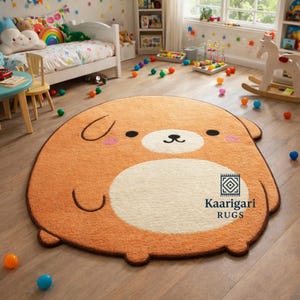 May include: A plush, cartoon-style rug in the shape of a dog. The rug features a light brown body with a white belly and face, black eyes, and pink cheeks. The rug has the text "Kaarigari RUGS".