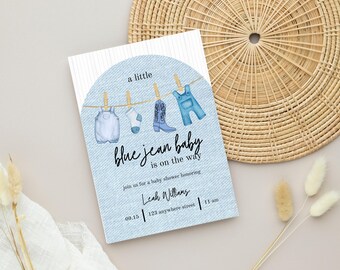 May include: Baby shower invitation with a blue jean theme. The invitation features watercolor illustrations of baby clothes hanging on a clothesline. The text reads "a little blue jean baby is on the way". Includes the date, time, and location.