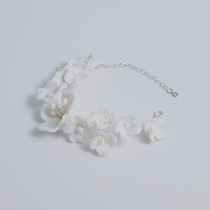 May include: A white floral bracelet with a silver chain and clasp. The bracelet features multiple white flower blossoms with pearl accents. The jewelry is designed for a delicate and feminine aesthetic.