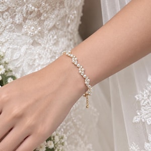 May include: A delicate gold-tone bracelet featuring a repeating pattern of small white pearls and clear sparkling crystals. The bracelet has a thin chain design with a small dangling charm at the clasp, creating a refined and elegant appearance.