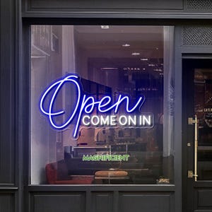 Könnte beinhalten: Ein Schaufenster zeigt ein Neonschild mit dem Wort "Open" in Schreibschrift, darunter "COME ON IN". Das Wort "MAGNIFICENT" steht darunter. Das Schild leuchtet in hellem Blau.