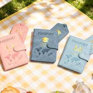 May include: A selection of passport covers and luggage tags in shades of pink and blue. The covers display the word "PASSPORT" in gold, with world maps and travel motifs. The luggage tags complement the covers with similar designs.
