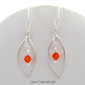 May include: Silver dangle earrings with a delicate leaf design and a small orange crystal in the center of each leaf.