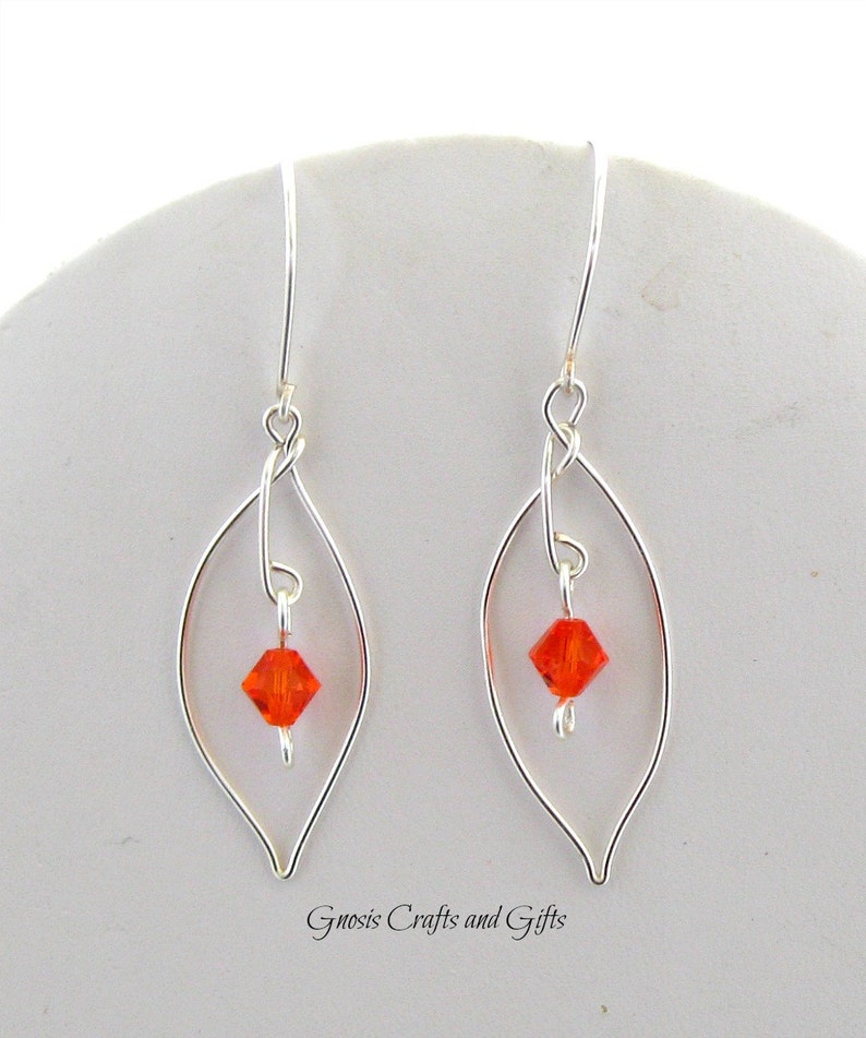 May include: Silver dangle earrings with a delicate leaf design and a small orange crystal in the center of each leaf.
