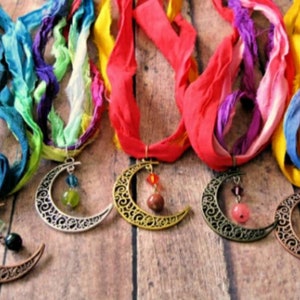 May include: Five handmade necklaces with crescent moon pendants and colorful silk ribbon. The pendants are in various metallic finishes and adorned with beads. The ribbons are in shades of blue, green, red, purple, and yellow.