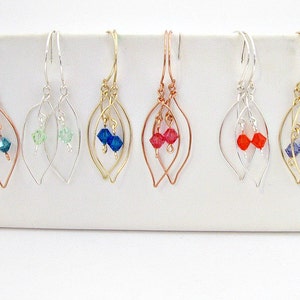 May include: Six pairs of leaf-shaped dangle earrings with crystal accents. The earrings are made with silver, gold, and copper wire. The crystals are in shades of blue, green, and red.