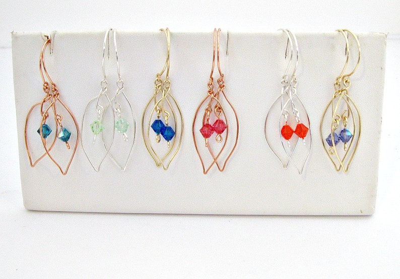 May include: Six pairs of leaf-shaped dangle earrings with crystal accents. The earrings are made with silver, gold, and copper wire. The crystals are in shades of blue, green, and red.