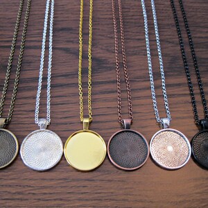 K&ouml;nnte beinhalten: Sieben verschiedene Ketten mit runden Anh&auml;ngern aus Metall. Die Anh&auml;nger sind in verschiedenen Farben, darunter Bronze, Silber, Gold, Kupfer und Schwarz.