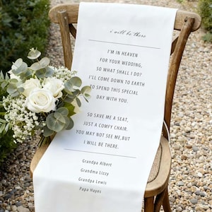 Puede incluir: Un camino de silla de boda blanco con texto negro que dice "I'm in Heaven for your wedding... I will be there." Un ramo de rosas blancas y vegetación descansa sobre la silla de madera, al aire libre.