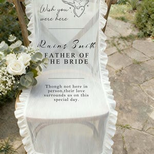 Op de afbeelding: Witte stoelsjerp met gerimpelde randen en verticale strepen. De sjerp heeft de tekst "Wish you were here", "Rains Smith, Father of the Bride", en een boodschap over liefde. Er is ook een duif- en hartafbeelding aanwezig.