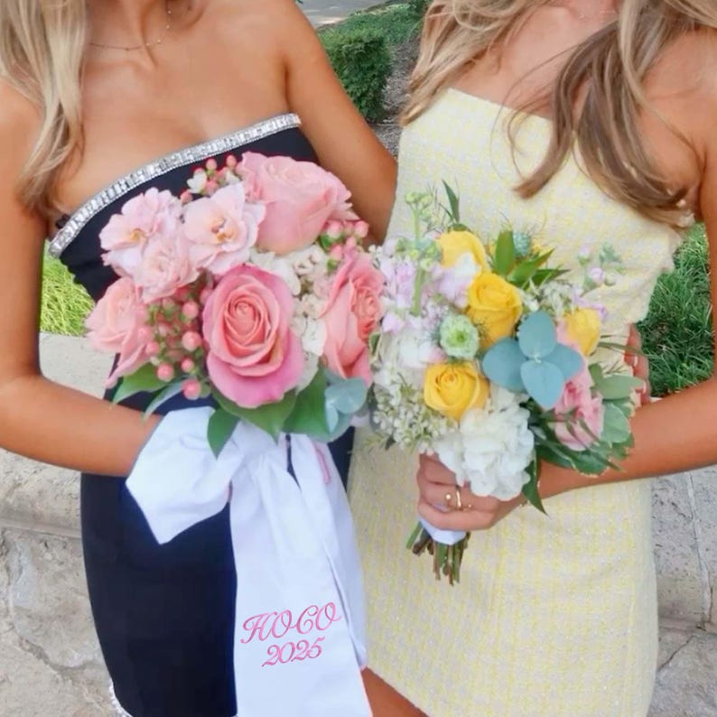 May include: Two women holding bouquets of flowers. One bouquet features pink roses and is paired with a black dress with a jeweled neckline and a white sash with pink text. The other bouquet has yellow and white flowers and is paired with a yellow dress.