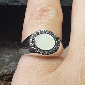 May include: A silver ring with a white oval stone surrounded by a black stone border.