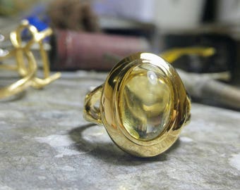 May include: A gold ring with a large, oval-shaped, clear yellow gemstone set in a bezel setting.