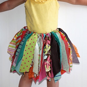 May include: A colorful fabric skirt with multiple strips of different patterns and colors, including green, pink, orange, brown, and blue. The skirt is tied at the waist and has a frayed edge.