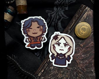 May include: Two character stickers with white borders. One features a cartoon man with blue hair and an orange and brown outfit. The other is a woman with blonde hair and a dark blue outfit. A gold-colored button and two small glass bottles are also visible.