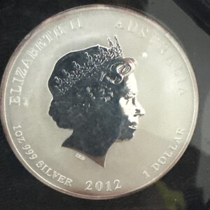 Może przedstawiać: Srebrna australijska moneta 1-dolarowa z 2012 roku. Moneta przedstawia profil kr&oacute;lowej Elżbiety II, napis "ELIZABETH II AUSTRALIA", "1 OZ 999 SILVER" i "1 DOLLAR".