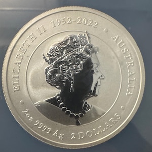 Może przedstawiać: Srebrna moneta z profilem ukoronowanej postaci, z napisem "ELIZABETH II 1952-2022 AUSTRALIA". Moneta zawiera r&oacute;wnież napis "2oz 9999 Ag 2 DOLLARS".