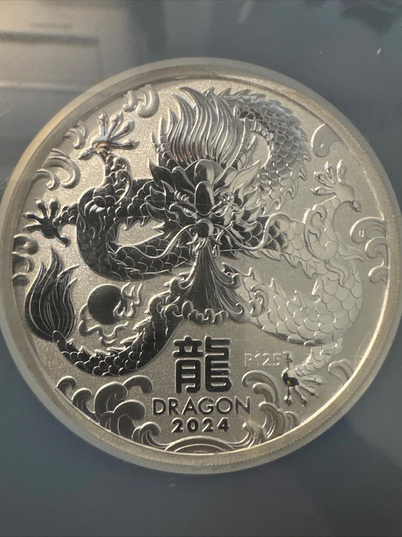 Może przedstawiać: Biały ceramiczny kubek z czarnym uchwytem i napisem "But First, Coffee" czarną, pogrubioną czcionką. Kubek stoi na białej powierzchni. Kubek ma około 10 cm wysokości.