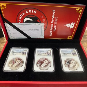 Peut inclure: Un coffret rouge contenant trois pièces Panda en argent, chacune dans un étui de protection. Les pièces présentent un motif de panda et le texte "10元". Le coffret comprend également un certificat et une couverture rouge avec le texte "Panda Coin" et "2020 Panda Storybook".