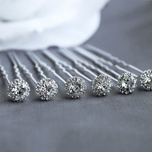 May include: Set of seven silver hair pins with clear rhinestone embellishments. Each pin has a round, clear rhinestone with smaller rhinestones surrounding it.