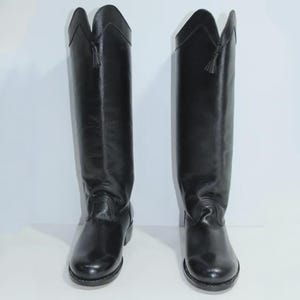 May include: A pair of black leather riding boots. The boots feature a decorative top with a small tassel and a rounded toe. Designed to be worn over the calf, they have a low heel. The boots are approximately 40 cm in height.