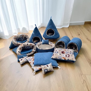 Könnte beinhalten: Eine Sammlung von Haustierbetten und Zubehör aus blauem Kord, bestehend aus zwei kegelförmigen Zelten, zwei Tunnelbetten, einem runden Bett mit kleinem Kissen und mehreren quadratischen Kissen mit einem Muster aus stilisierten Bären auf beigem Grund.