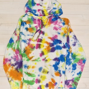 May include: A long-sleeve hooded sweatshirt featuring a vibrant tie-dye pattern with splashes of blue, pink, yellow, green, orange, and purple on a white base. The garment includes a front kangaroo pocket, a drawstring hood, and ribbed cuffs.
