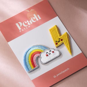 May include: Embroidered patches including a rainbow, a smiling cloud, and a yellow lightning bolt with a face. The patches are on a pink and white card with the "Peach Patch" logo.
