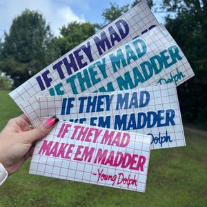 May include: A set of four rectangular vinyl decals featuring the text IF THEY MAD MAKE EM MADDER -Young Dolph in purple, teal, blue, and pink. Each decal is printed on a white grid transfer paper backing, displaying bold sans-serif lettering.