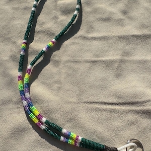 May include: Handmade beaded lanyard with a dark green base, accented with white stripes and sections of rainbow-colored beads. The lanyard has a white cord and a silver key ring attached to the end.