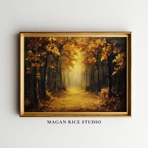 Puede incluir: Un cuadro de paisaje en un marco dorado que representa un sendero forestal en otoño con follaje amarillo dorado y marrón en los árboles. La escena presenta una luz brillante y resplandeciente al final del camino. El texto MAGAN RICE STUDIO es visible.