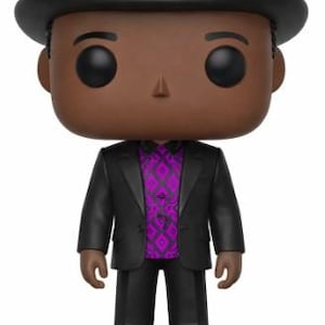 Może przedstawiać: Figurka winylowa Funko Pop przedstawiająca osobę w czarnym garniturze i kapeluszu, z fioletową gitarą na kapeluszu. Figurka ma brązową karnację i fioletową koszulę we wzory. Figurka stoi na czarnej podstawie.