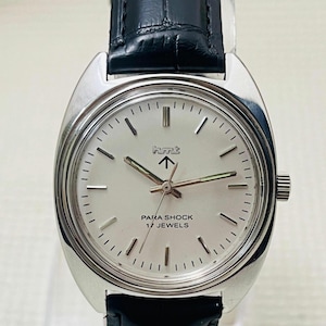 May include: Silver-toned wristwatch with a white face, black leather band, and the text "PARA SHOCK 17 JEWELS." The watch has a classic design with a round face and a black leather strap. The watch face has a logo and arrow.